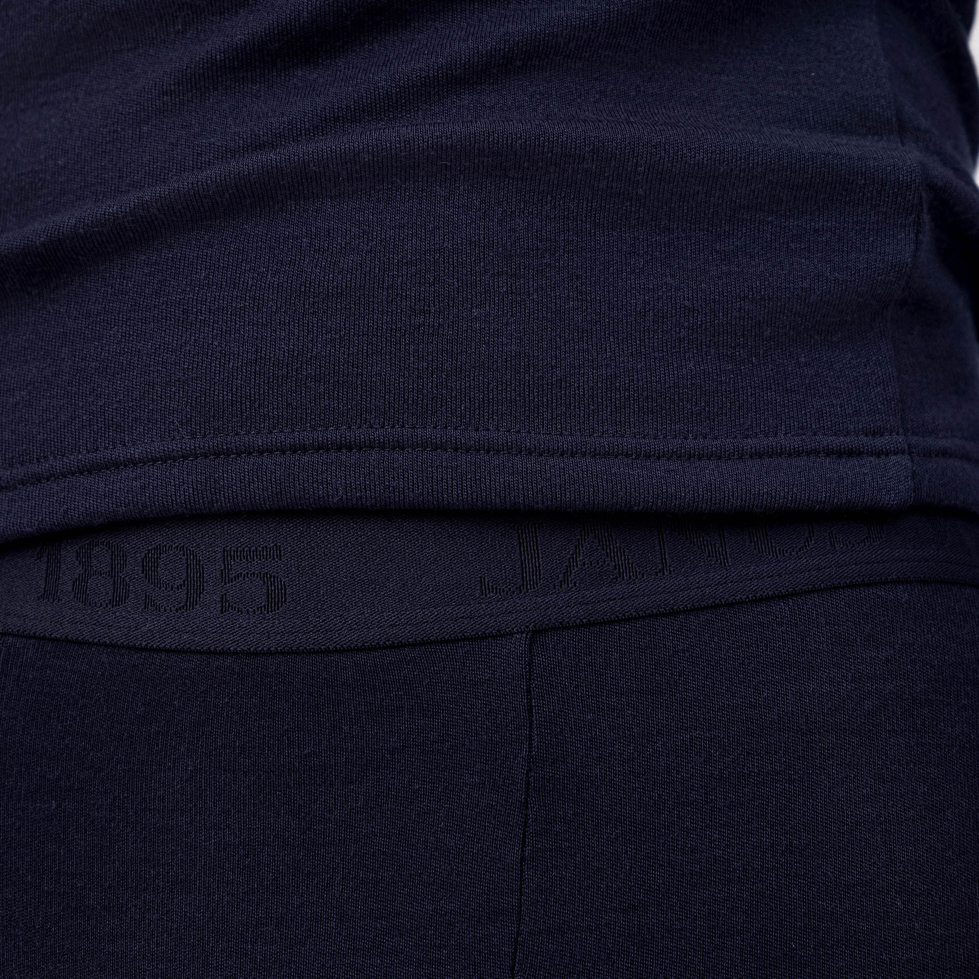 Close-up of a person wearing Leggings Merino – AirWool 260 Men, showing the waistband with "1895" and subtle text. The soft merino wool knit provides warmth and breathability.