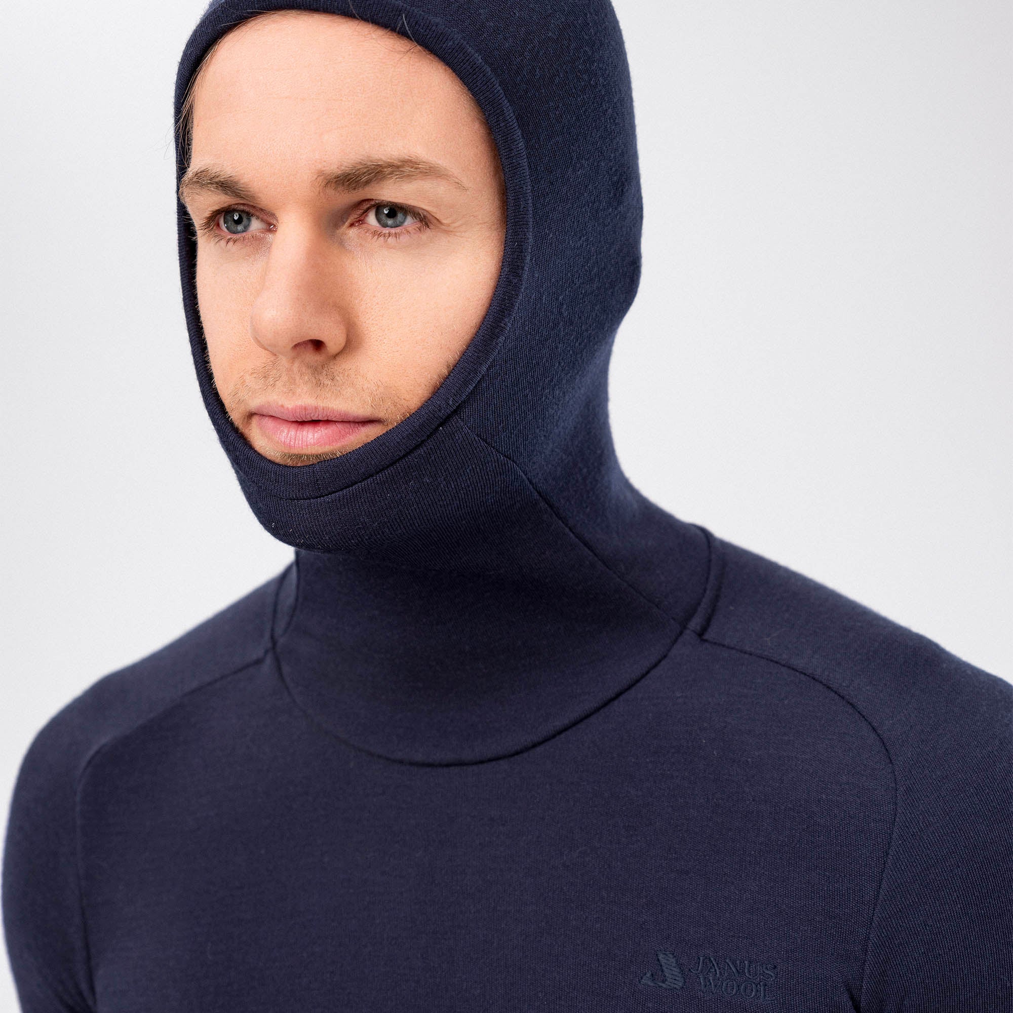 A man wears the Hooded Jersey Merino – AirWool 260 Men in navy blue, a close-fitting, breathable merino wool hoodie, looking slightly to the side against a plain light background.