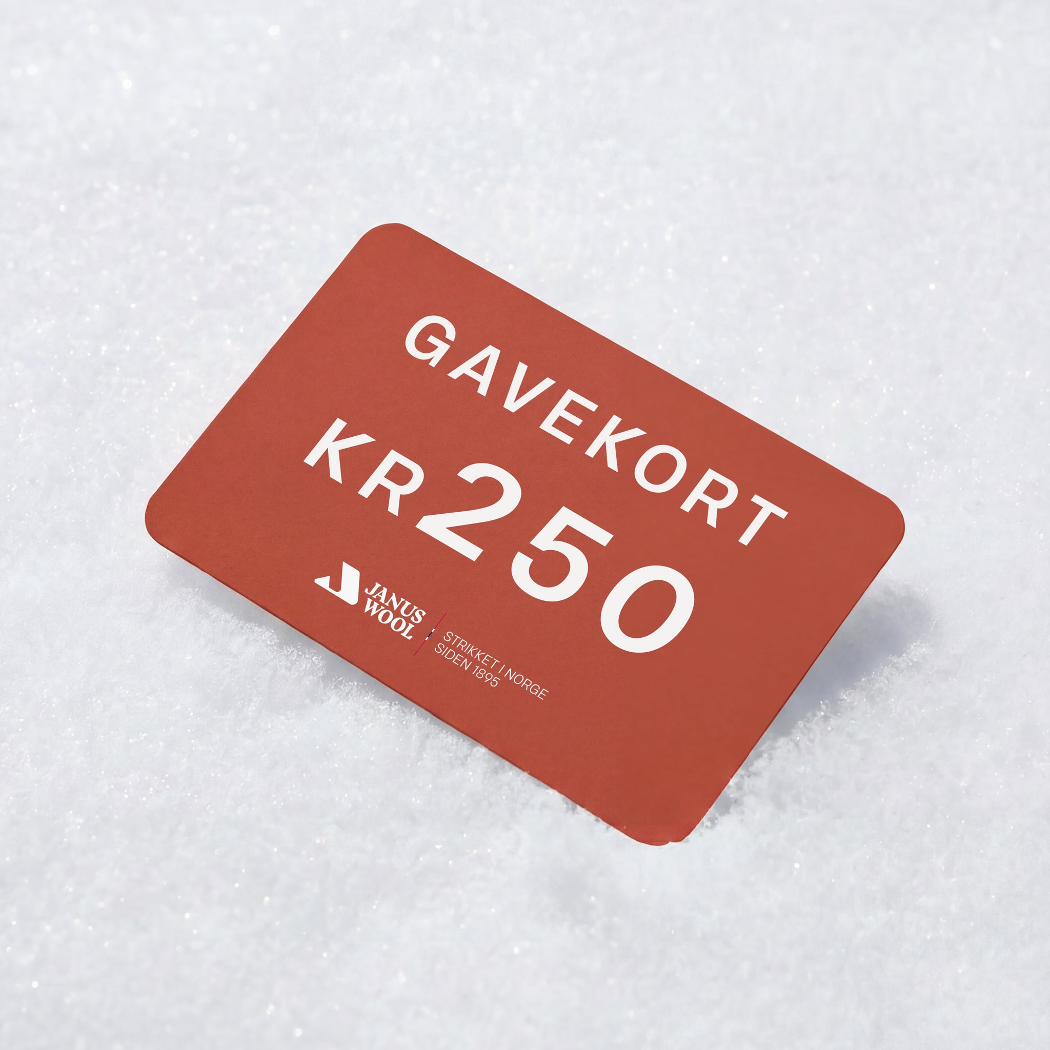 A red Janus Wool Gift Card labeled GAVEKORT KR 250 from Janus Wool rests on white snow—ideal for merino wool fans, showcasing its 250 Norwegian kroner value.
