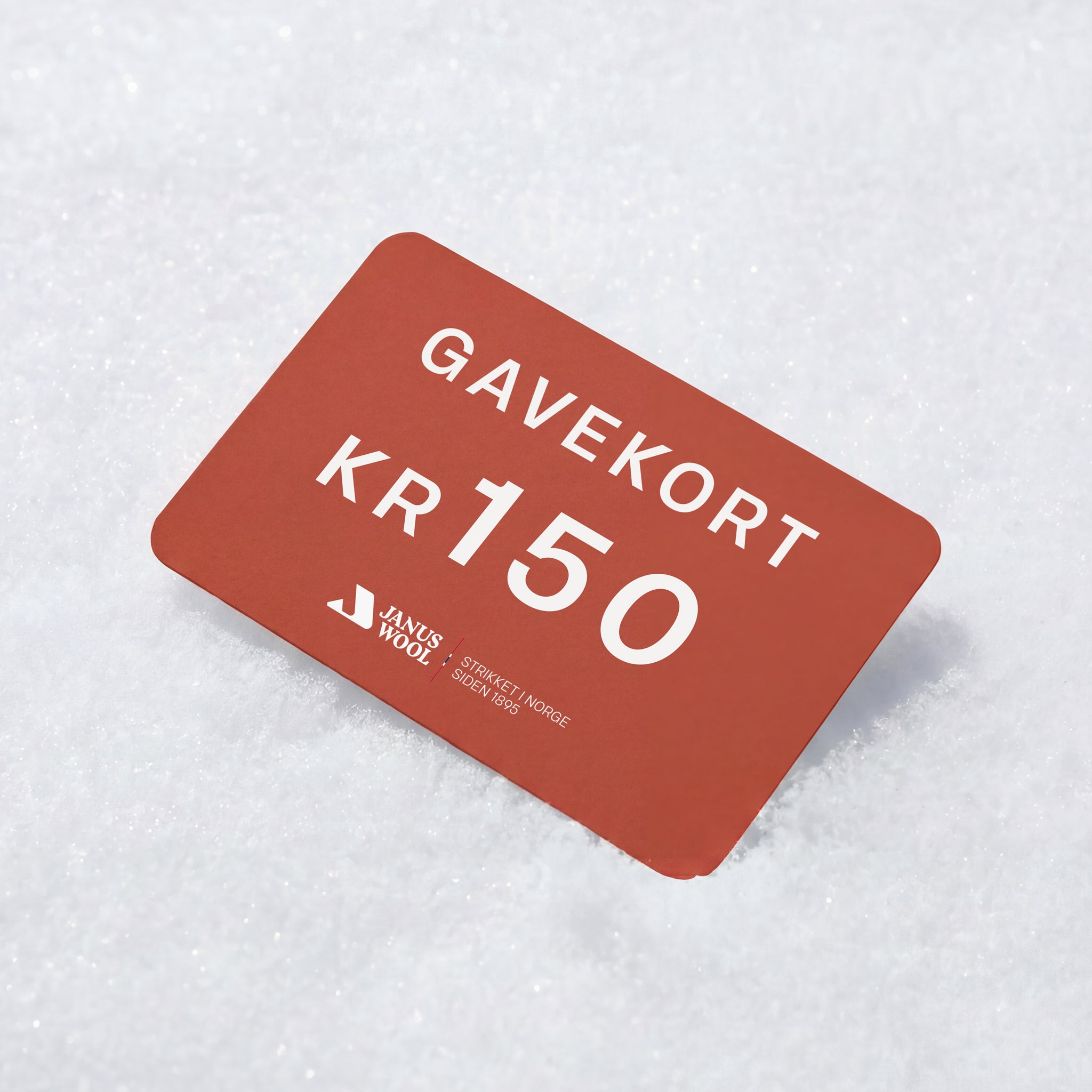 A Janus Wool Gift Card featuring "GAVEKORT KR150" in red with the logo, rests on white snow—a perfect gift for merino wool fans.