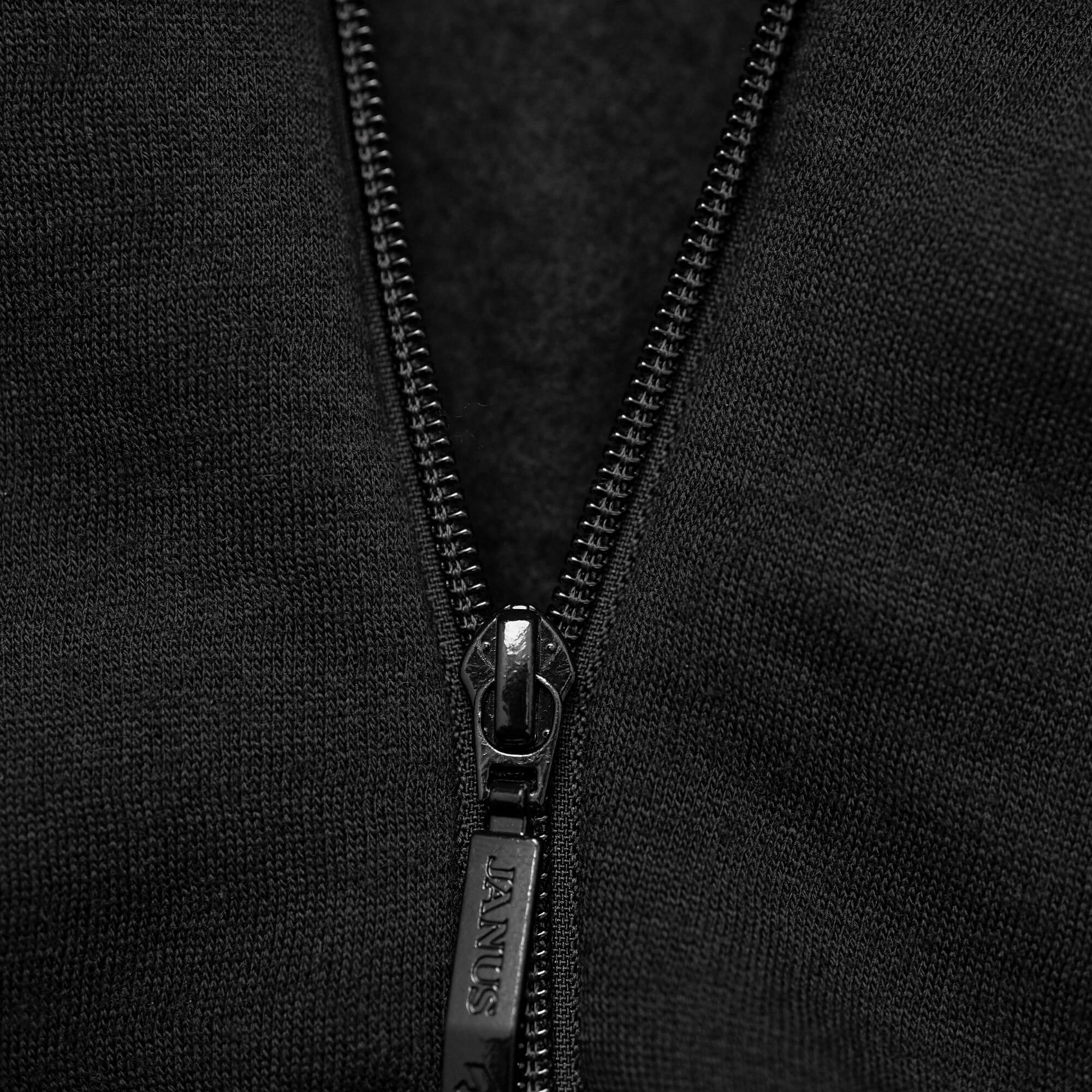 Close-up of a partially unzipped black zipper on dark fabric, part of the Jacket Merino – AirWool 350 Women, with the zipper pull engraved with the word JEANS.