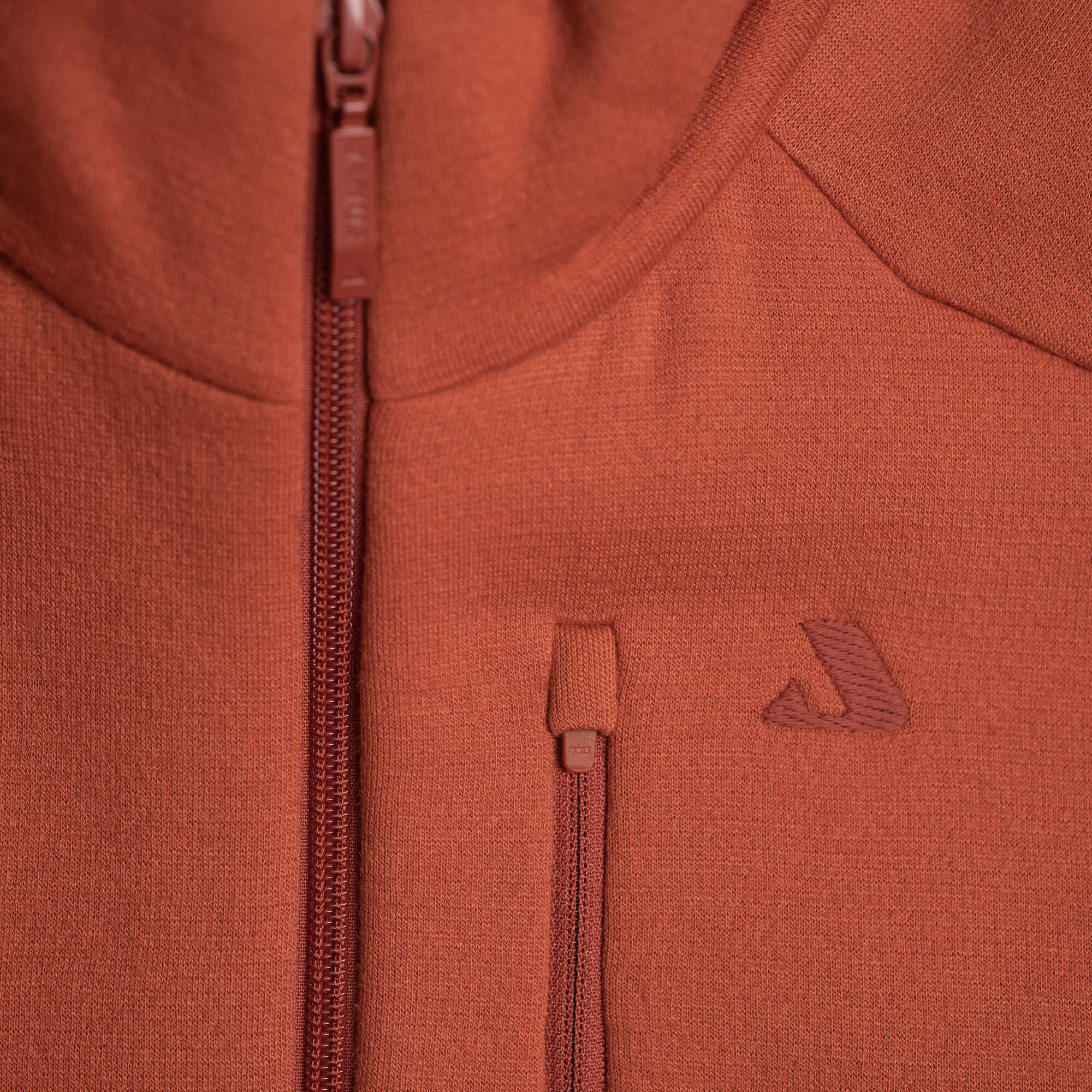 Close-up of the Vest Merino – AirWool 350 Men: a rust-colored zip-up vest with a vertical zippered pocket, main zipper, and subtle embroidered logo on warm, breathable textured fabric.