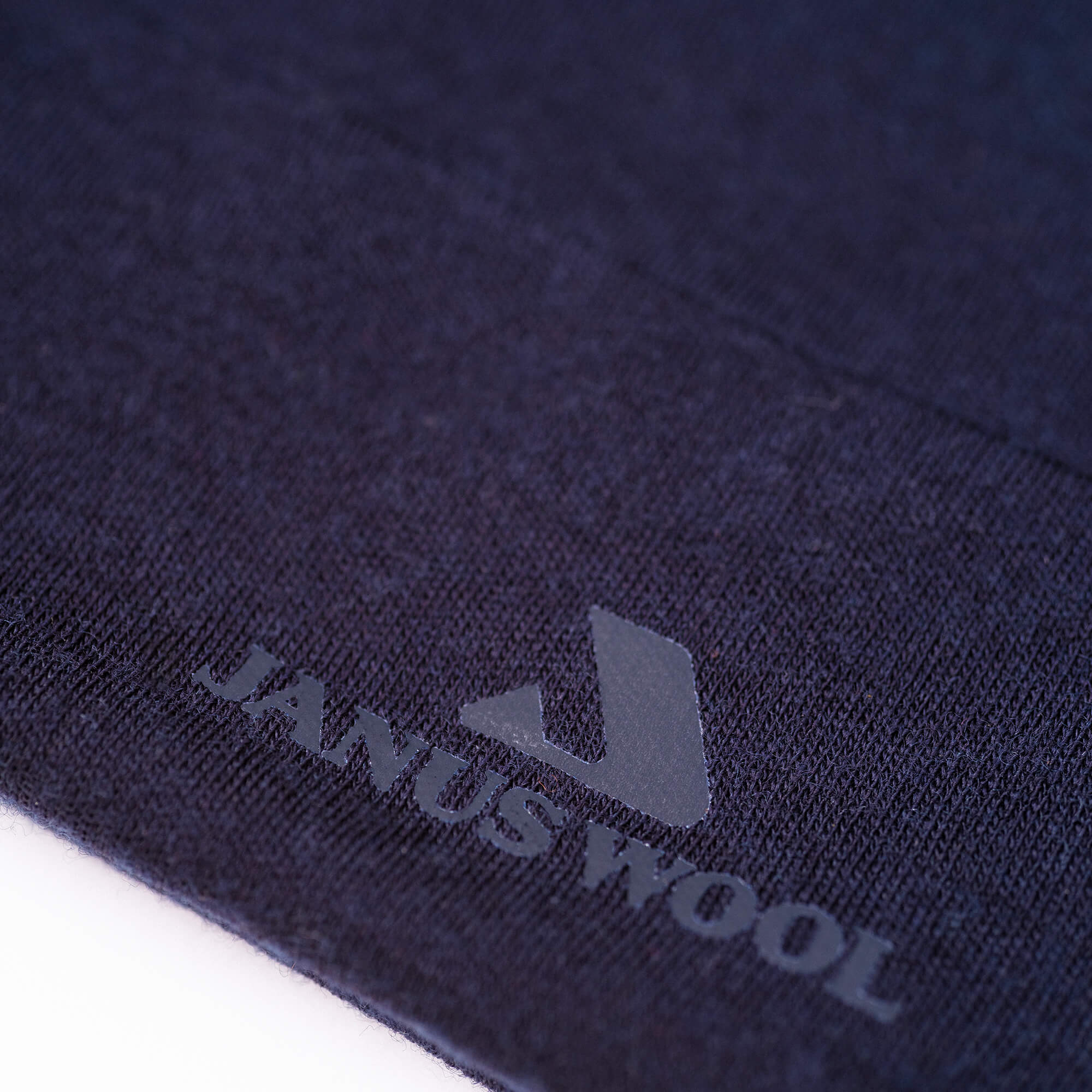 Close-up of the Beanie – Classic Merino 215 in navy blue, featuring the WOOL logo and a stylized J in gray, showcasing its warm, breathable merino wool fabric.