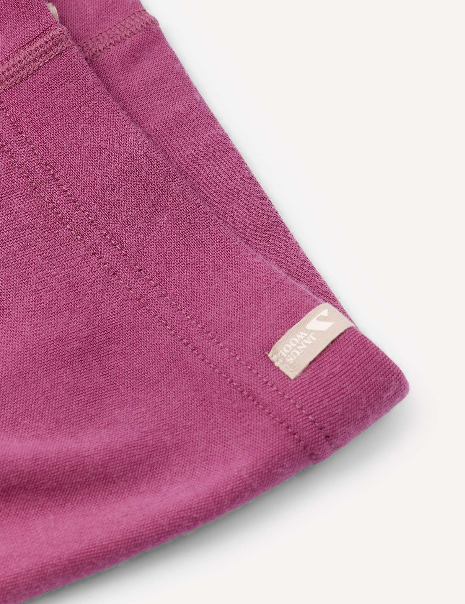 Close-up of the Merino Kids AirWool Leggings in magenta brushed wool, featuring visible stitching and a small beige tag. The soft fabric is displayed against a light, neutral background.