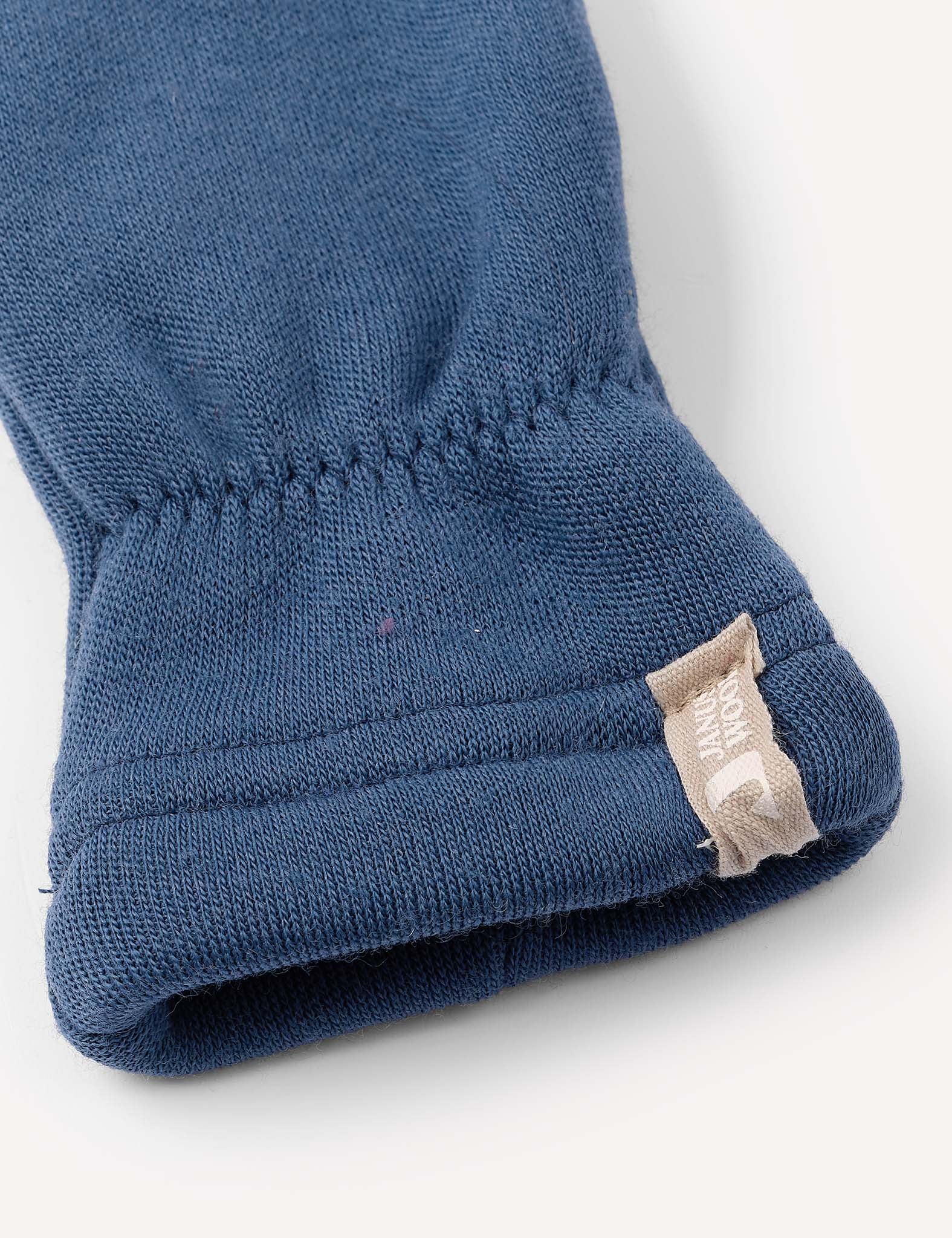 Close-up of a blue fabric sleeve with an elastic cuff and a small beige tag stitched into the seam, featuring white text and a partial logo—crafted from ultra-soft Merino Kids AirWool 260 for ultimate comfort, just like your favorite warm Mittens.