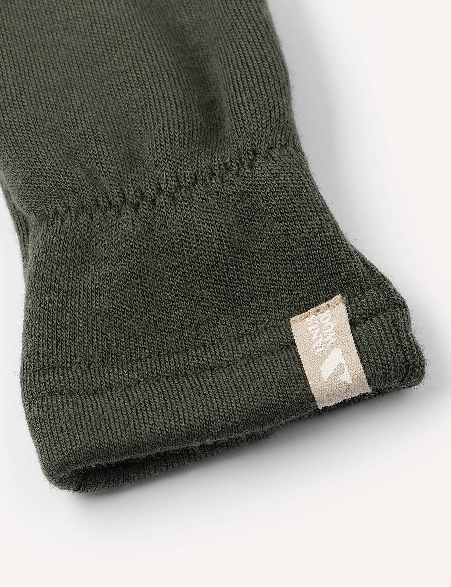 Close-up of the cuff of a dark green Merino Kids AirWool mitten, featuring a small beige fabric tag sewn onto the edge with a white logo and text.