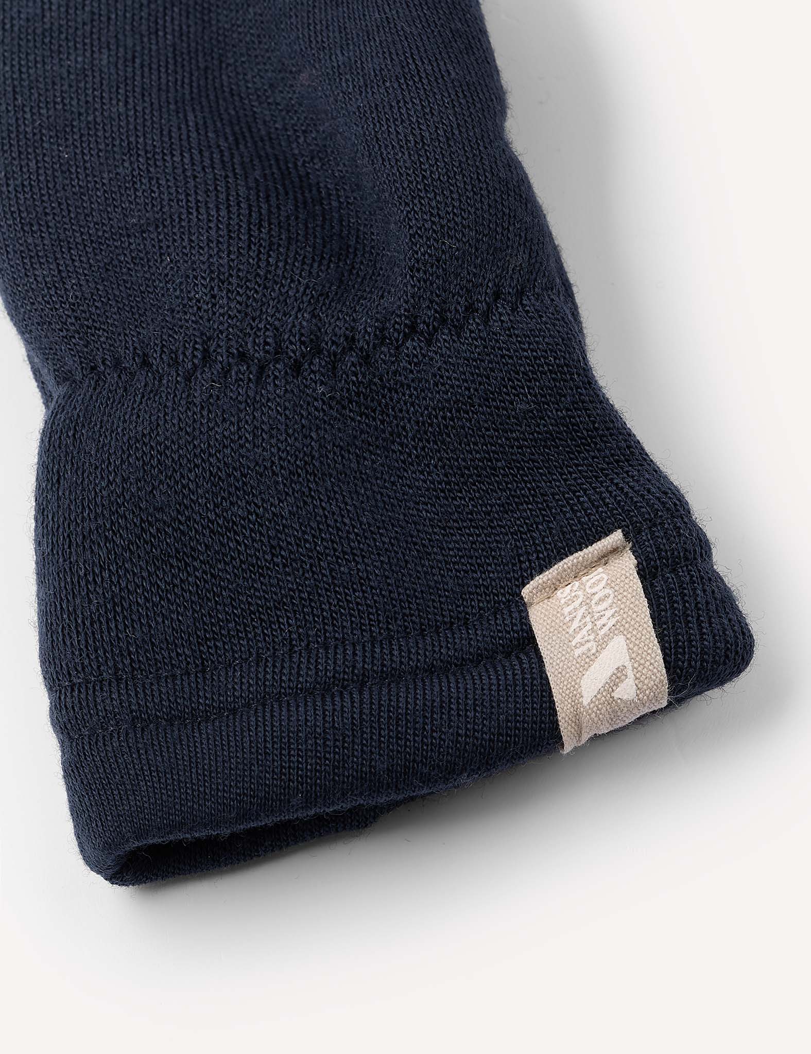 Close-up of the cuff of a navy blue Merino Kids AirWool mitten, featuring a small beige tag with white text. The background is a plain, light color.