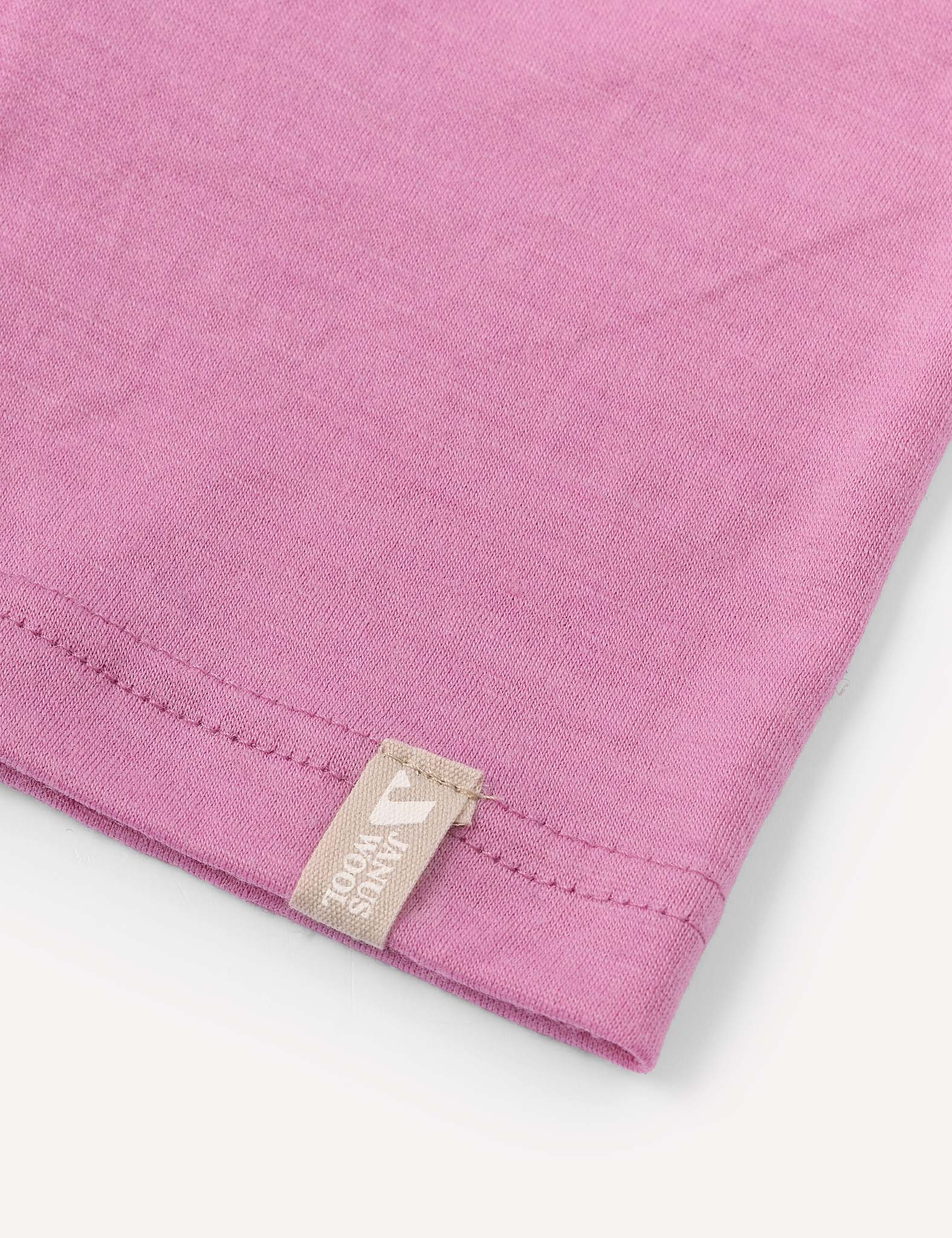 A close-up of the corner of the pink Merino Kids Light Neckwarmer, made from merino wool, features a beige tag with white text and a small design sewn into the seam. The background is white.