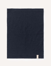 A neatly folded square piece of navy Neckwarmer – Merino Kids Light, featuring a small beige tag in the bottom right corner, placed on a light background.