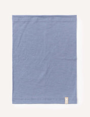 A neatly folded square piece of the Neckwarmer – Merino Kids Light in the color Troposphere, featuring a small beige tag on the bottom right corner, set against a plain off-white background.