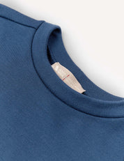 Close-up of the Pullover – Merino Kids AirWool in blue, highlighting the collar and a white inner label with red and gray text, set against a plain white background.