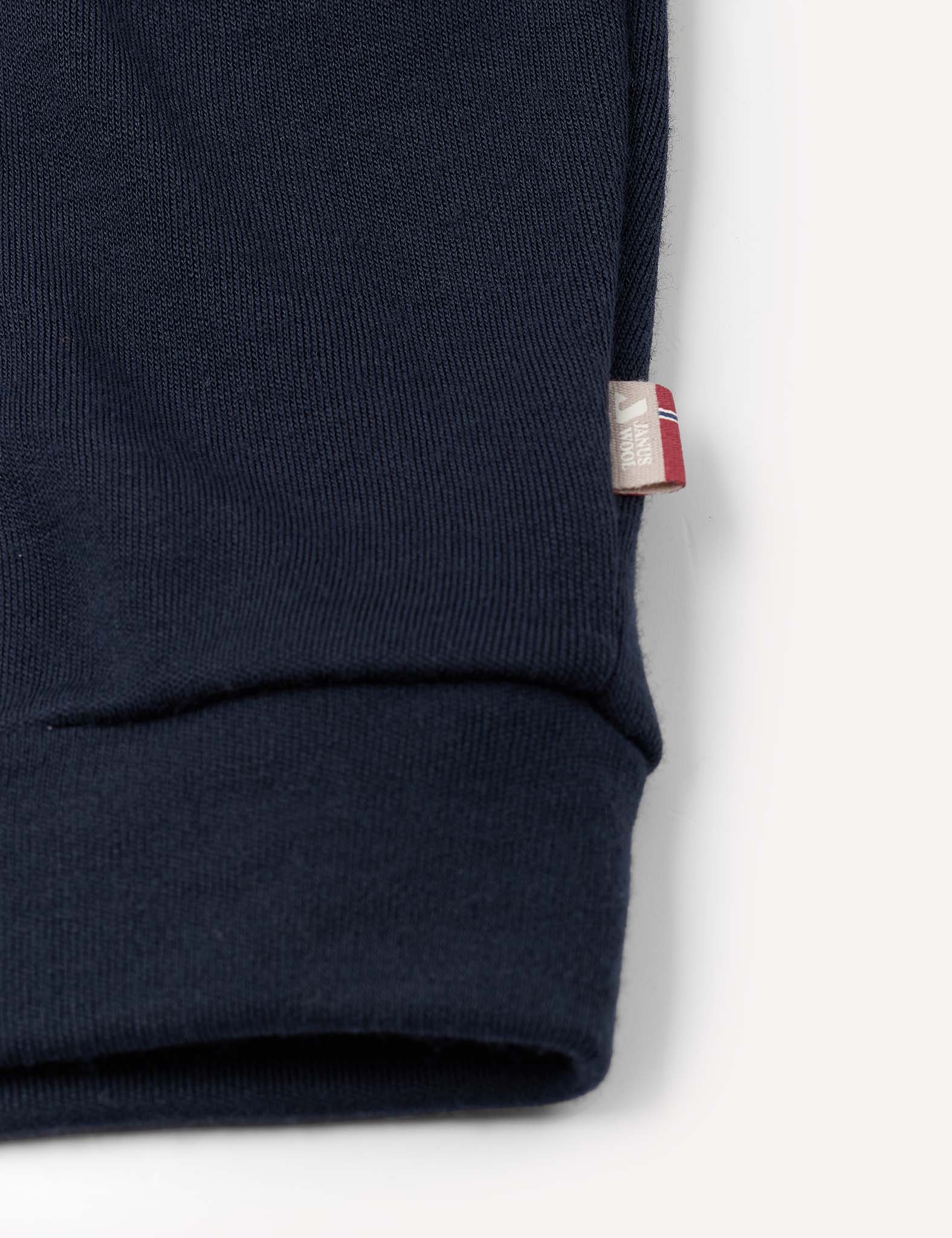 Close-up of the navy blue cuff of the Pullover – Merino Kids AirWool sweater, featuring a small fabric tag on the seam with red, white, and blue details.