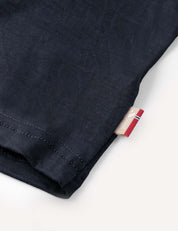 Close-up of the hem of the T-Shirt – Merino Kids Light in dark blue merino wool, featuring a small beige tag with red, white, and blue details stitched into the side seam. The fabric delivers natural temperature regulation and all-day comfort.